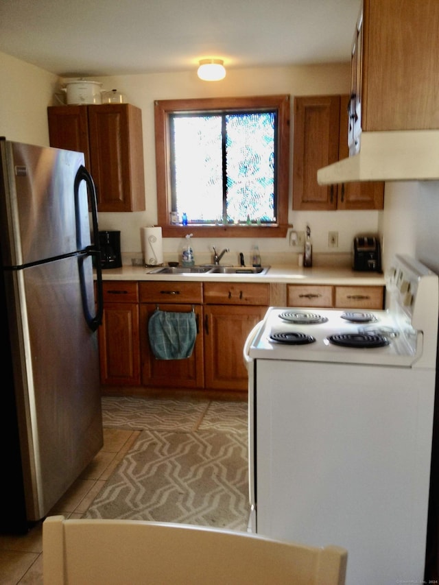 kitchen with stainless steel refrigerator, sink, white range, extractor fan, and light tile patterned floors