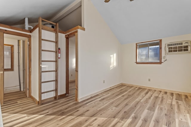 empty room featuring vaulted ceiling with beams, an AC wall unit, and light hardwood / wood-style flooring