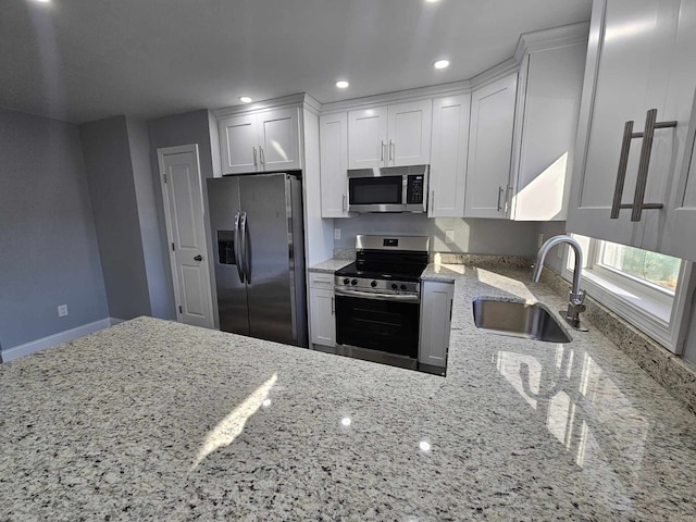 kitchen with light stone countertops, sink, kitchen peninsula, white cabinets, and appliances with stainless steel finishes