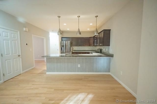 kitchen with kitchen peninsula, stainless steel refrigerator with ice dispenser, dark brown cabinets, light hardwood / wood-style flooring, and hanging light fixtures