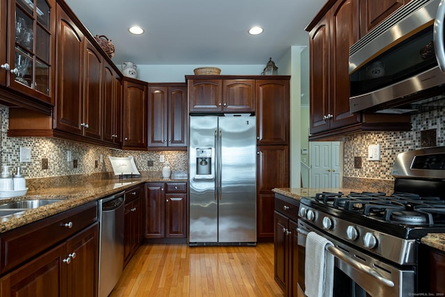 kitchen with decorative backsplash, dark brown cabinets, stainless steel appliances, stone countertops, and light hardwood / wood-style floors