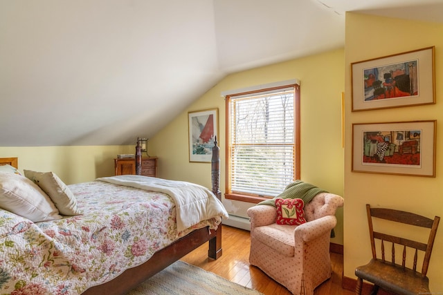 bedroom with light wood-type flooring, baseboard heating, and vaulted ceiling