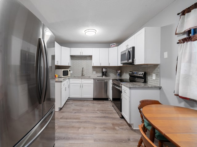 kitchen featuring light stone countertops, white cabinetry, sink, stainless steel appliances, and light hardwood / wood-style flooring