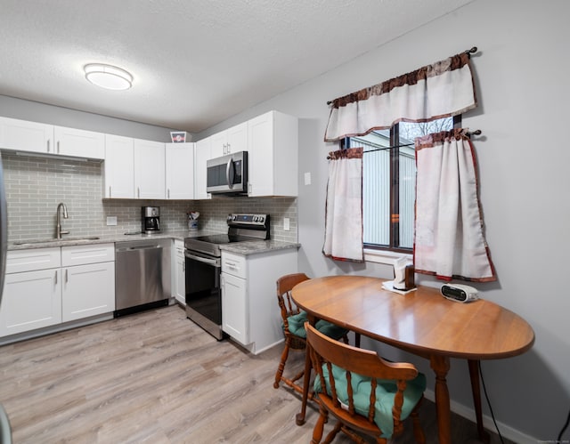 kitchen featuring white cabinets, light hardwood / wood-style floors, light stone countertops, and appliances with stainless steel finishes