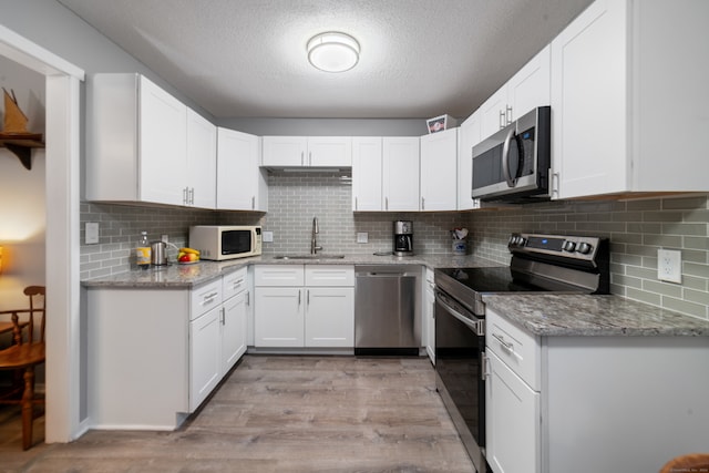 kitchen with light stone counters, stainless steel appliances, sink, light hardwood / wood-style floors, and white cabinetry