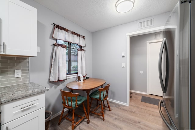 kitchen featuring light stone countertops, stainless steel fridge, tasteful backsplash, white cabinets, and light hardwood / wood-style floors