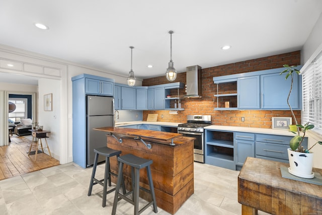 kitchen featuring wall chimney exhaust hood, stainless steel appliances, blue cabinetry, light hardwood / wood-style flooring, and a center island