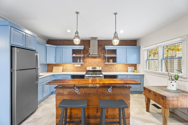 kitchen with blue cabinetry, a breakfast bar, stainless steel appliances, and wall chimney range hood