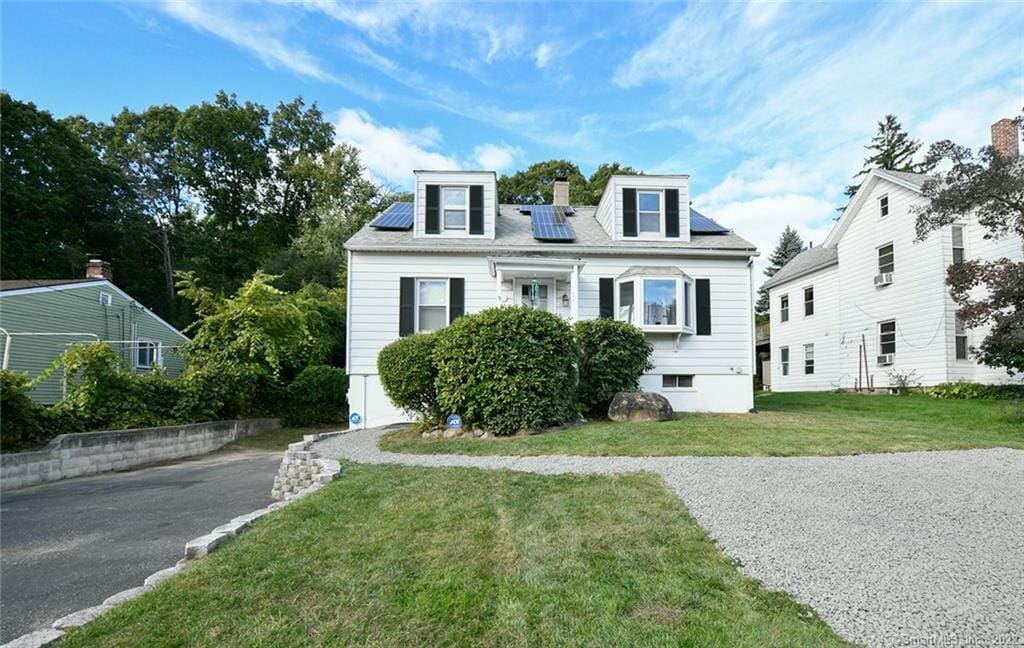 cape cod home featuring solar panels and a front lawn