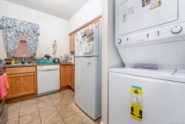 kitchen with a textured ceiling, white appliances, stacked washer and dryer, and light tile patterned floors