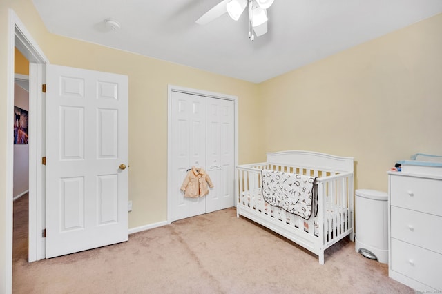 bedroom with a crib, light carpet, a closet, and ceiling fan