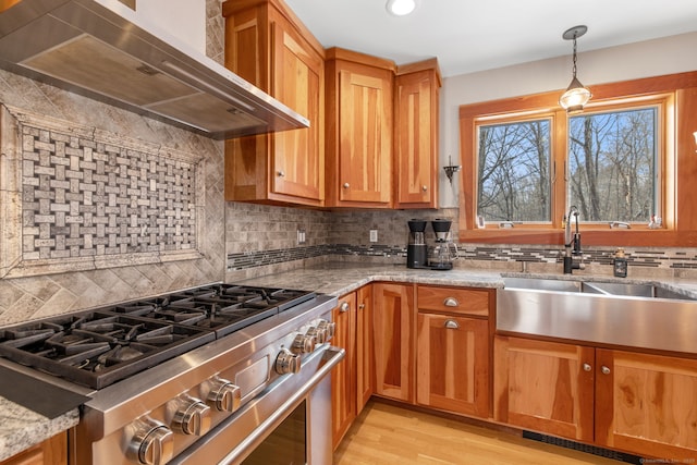 kitchen featuring wall chimney exhaust hood, sink, stainless steel range with gas cooktop, pendant lighting, and light stone countertops