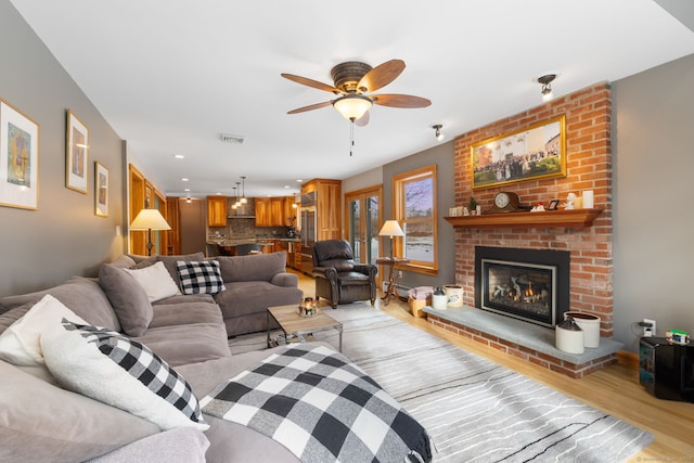 living room with ceiling fan, a fireplace, light hardwood / wood-style flooring, and a baseboard radiator