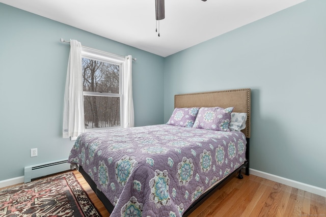 bedroom featuring ceiling fan, light wood-type flooring, and baseboard heating