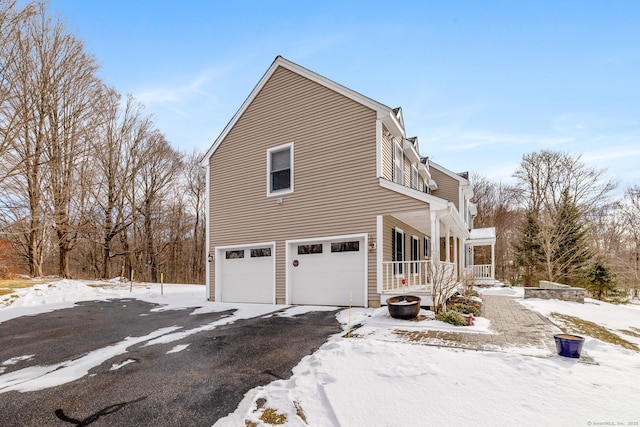 snow covered property with a garage and covered porch