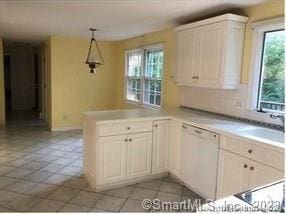 kitchen with kitchen peninsula, white dishwasher, pendant lighting, white cabinets, and light tile patterned flooring