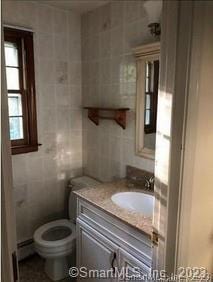 bathroom featuring a baseboard heating unit, vanity, tile walls, and toilet