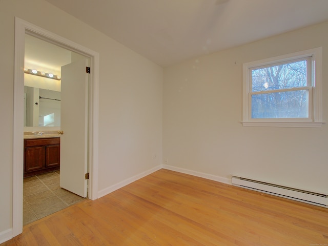 empty room with light hardwood / wood-style flooring, baseboard heating, and sink