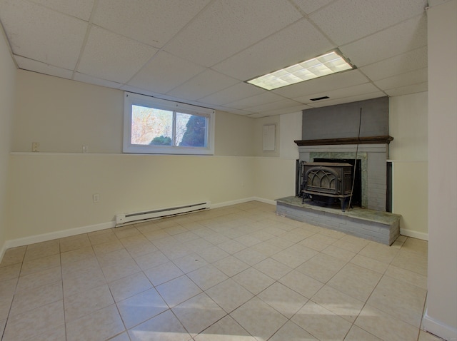 basement featuring a baseboard radiator, a wood stove, and a drop ceiling