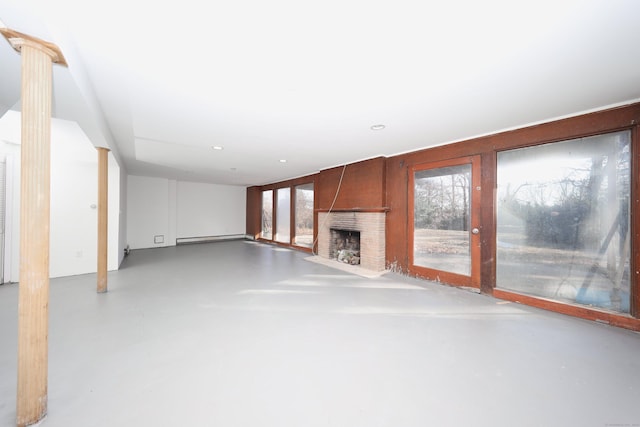 unfurnished living room with concrete flooring, a baseboard heating unit, and a brick fireplace