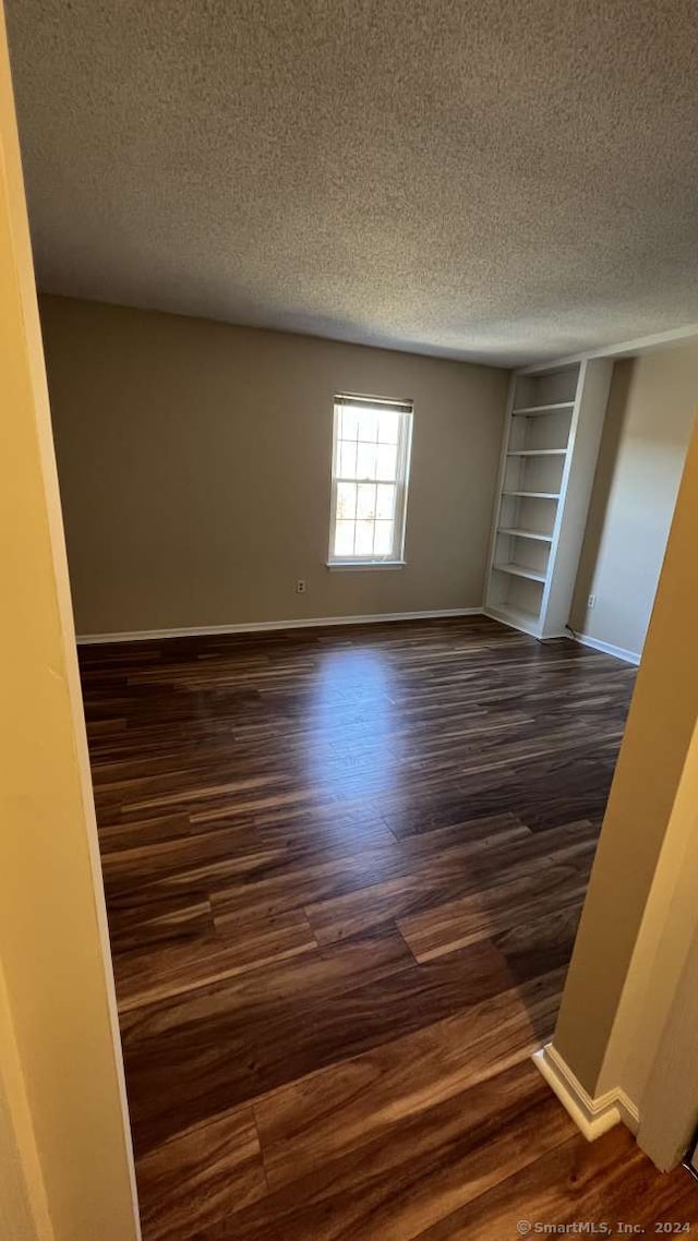 unfurnished room with a textured ceiling and dark hardwood / wood-style floors