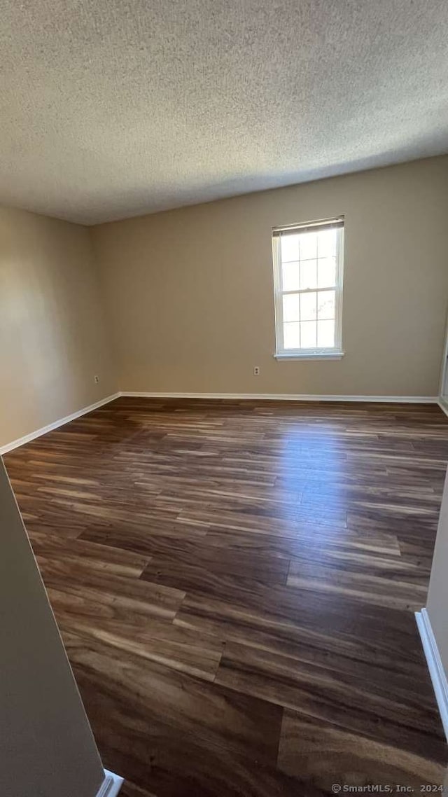 empty room with a textured ceiling and dark hardwood / wood-style flooring