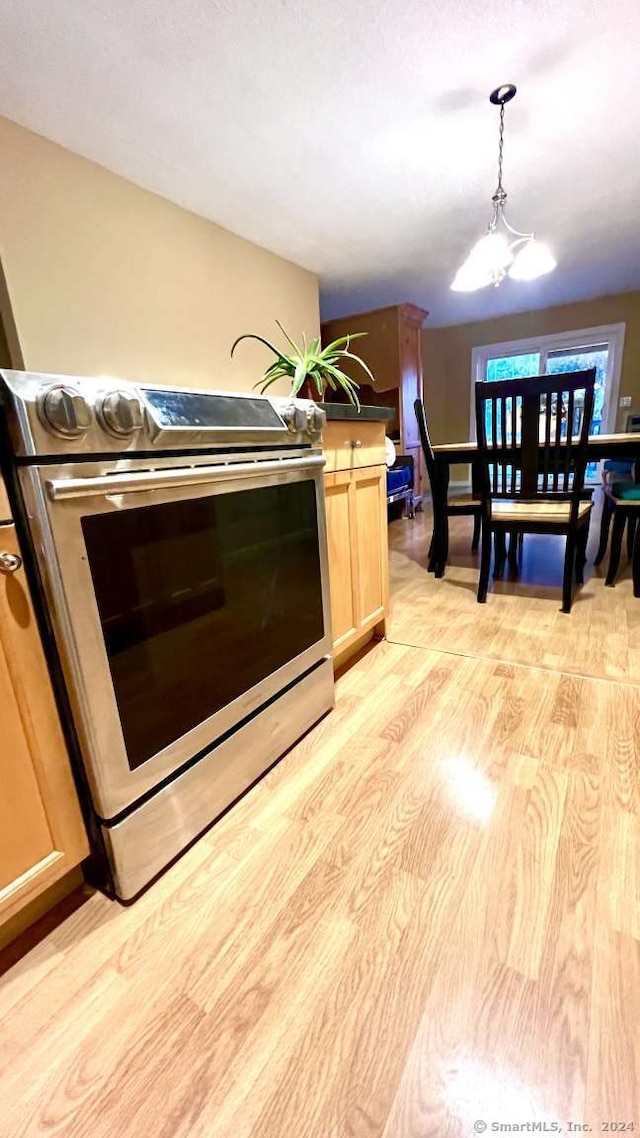 kitchen featuring stainless steel electric range oven, light brown cabinets, light hardwood / wood-style flooring, pendant lighting, and a chandelier