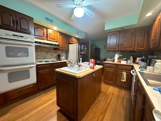 kitchen with a center island, white appliances, backsplash, light hardwood / wood-style flooring, and ceiling fan