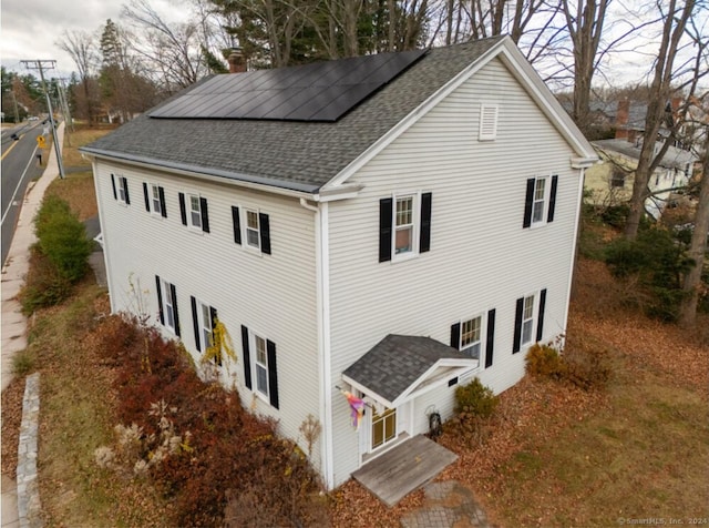 view of side of property with a shingled roof, a chimney, and roof mounted solar panels