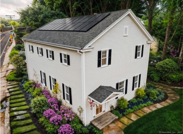 view of home's exterior with a shingled roof and roof mounted solar panels