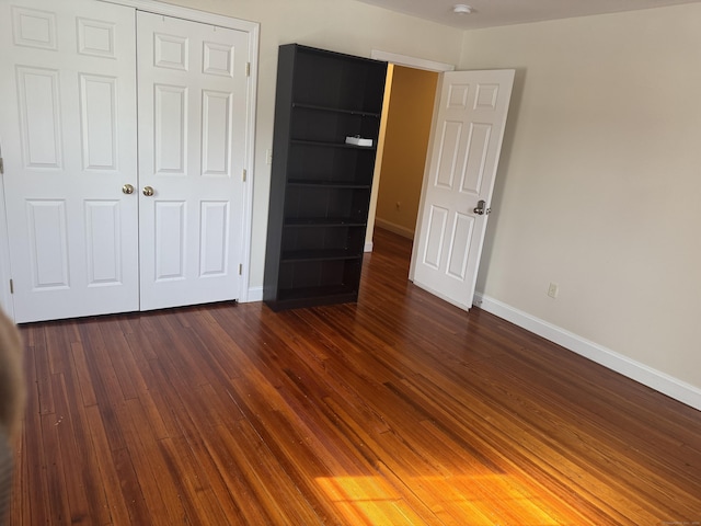 unfurnished bedroom featuring a closet, dark wood finished floors, and baseboards