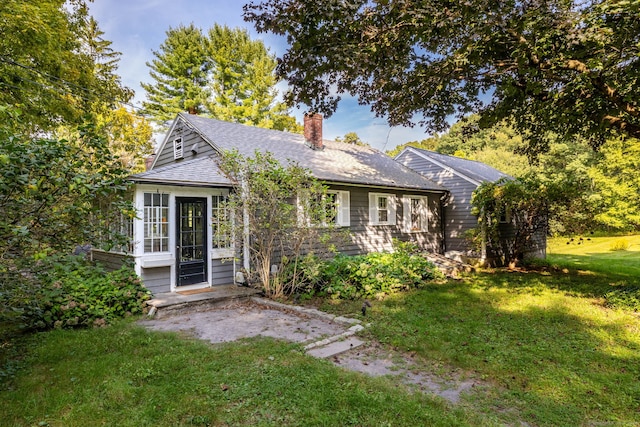 bungalow-style home with roof with shingles, a chimney, and a front yard