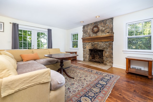 living room featuring a stone fireplace, dark wood-type flooring, and french doors