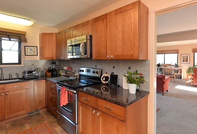 kitchen with dark colored carpet, sink, decorative backsplash, dark stone countertops, and stainless steel appliances