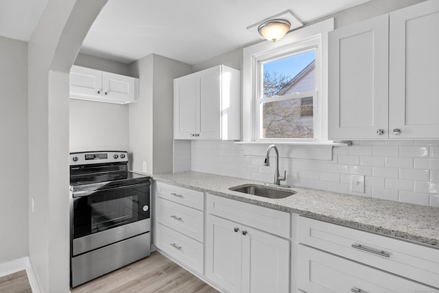 kitchen with sink, stainless steel stove, light stone counters, white cabinets, and light wood-type flooring