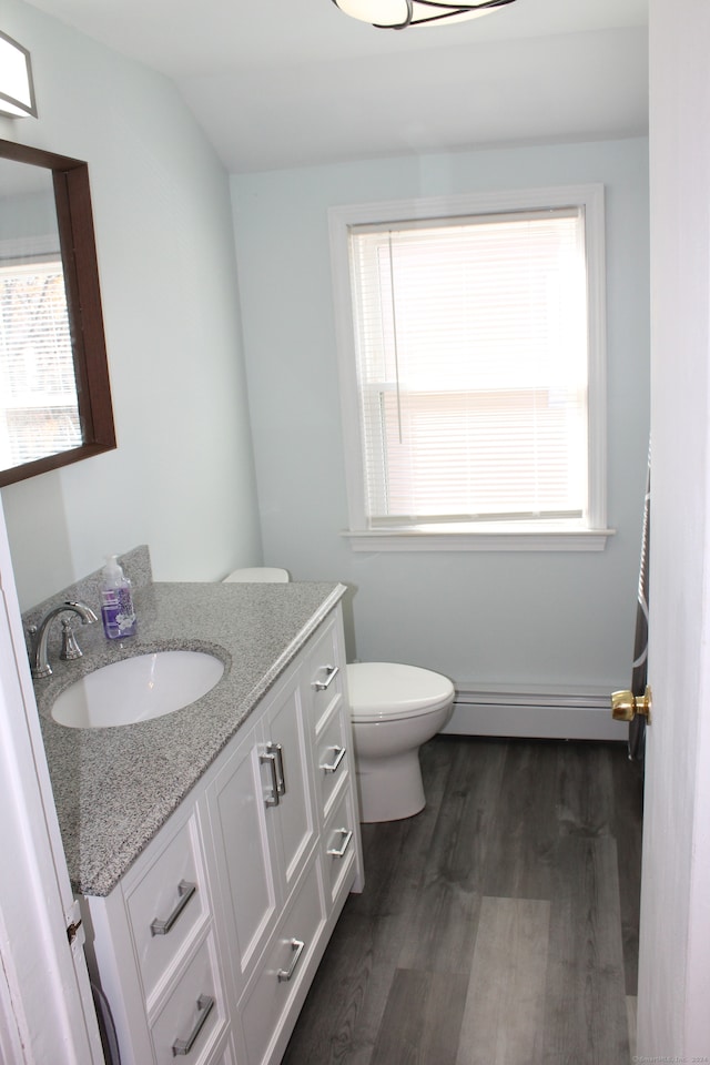 bathroom featuring a healthy amount of sunlight, toilet, wood-type flooring, and a baseboard heating unit