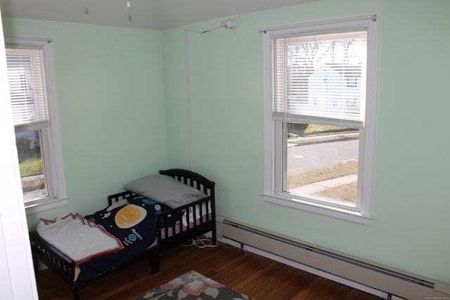 bedroom with baseboard heating, multiple windows, dark wood-type flooring, and a crib