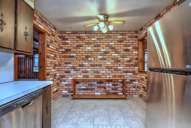 kitchen with ceiling fan, light tile patterned floors, stainless steel appliances, and brick wall