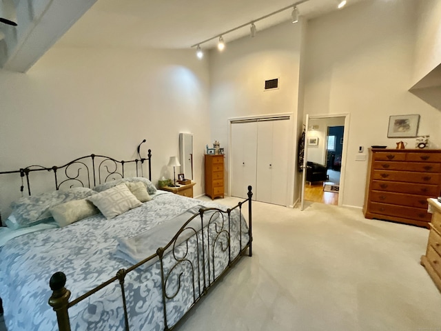 bedroom featuring track lighting, light colored carpet, a high ceiling, and a closet