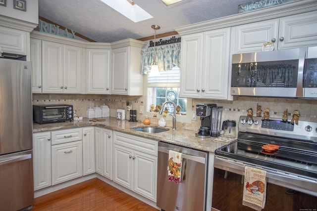 kitchen with appliances with stainless steel finishes, sink, white cabinets, and light stone counters