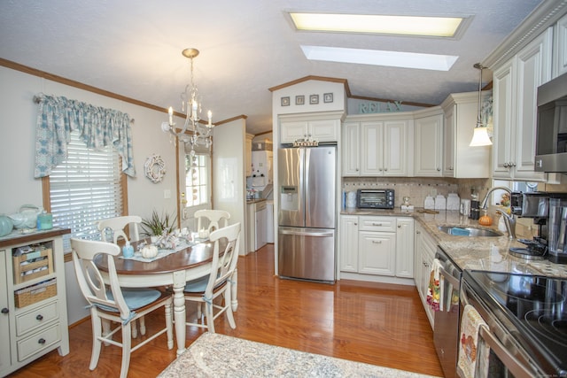 kitchen featuring appliances with stainless steel finishes, vaulted ceiling with skylight, wood-type flooring, light stone countertops, and decorative light fixtures