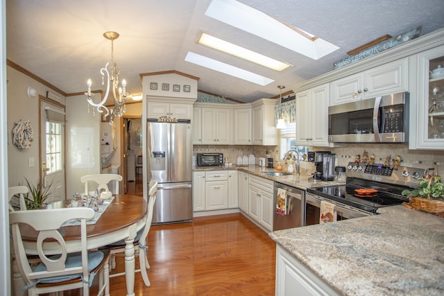 kitchen featuring pendant lighting, sink, lofted ceiling with skylight, stainless steel appliances, and light stone countertops