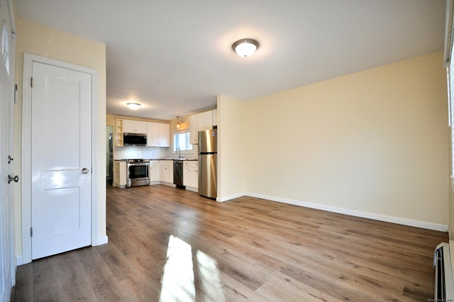 kitchen with white cabinets, stainless steel appliances, baseboard heating, and light hardwood / wood-style floors