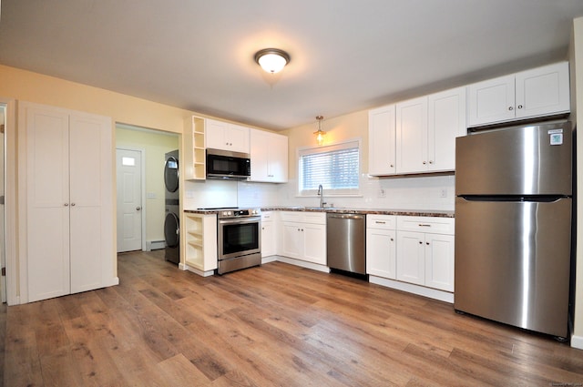 kitchen with backsplash, stainless steel appliances, stacked washer / dryer, light hardwood / wood-style floors, and white cabinetry