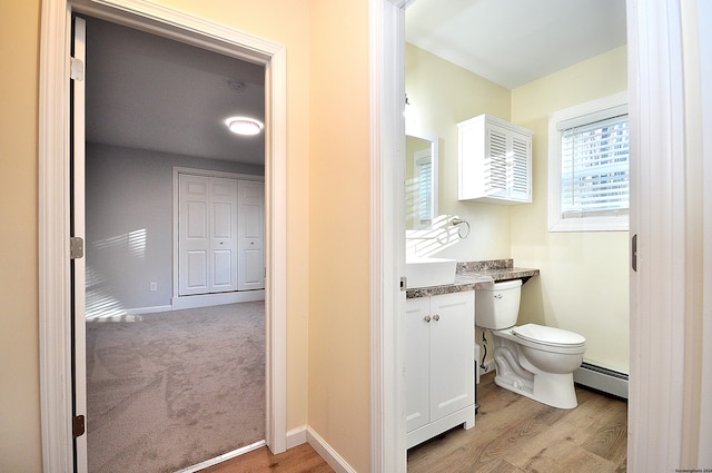 bathroom with toilet, vanity, wood-type flooring, and a baseboard heating unit