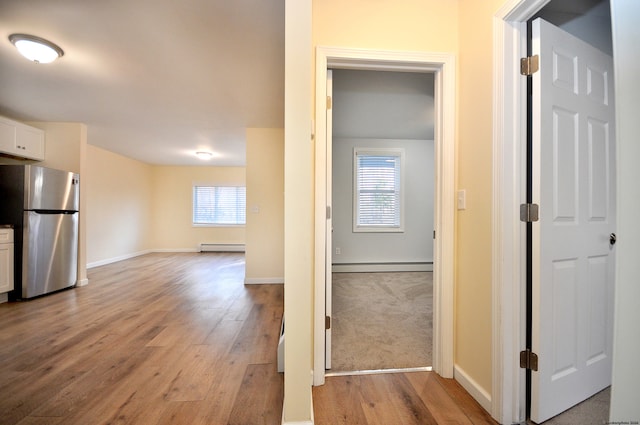 hallway featuring a healthy amount of sunlight, a baseboard radiator, and light hardwood / wood-style floors