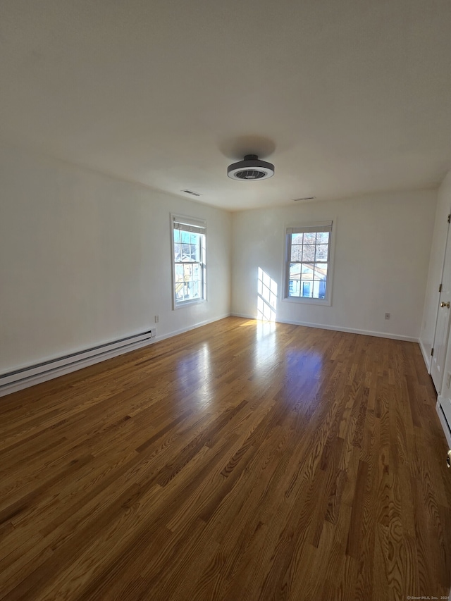 unfurnished room featuring dark hardwood / wood-style flooring, plenty of natural light, and a baseboard heating unit