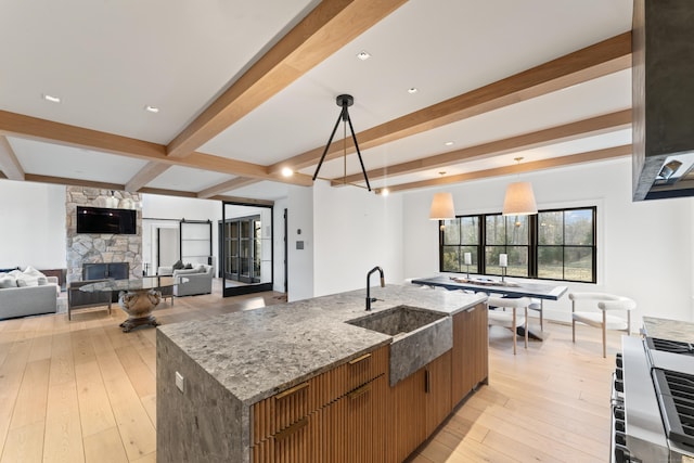 kitchen with light stone counters, sink, a stone fireplace, hanging light fixtures, and a large island