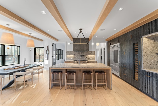 kitchen featuring tasteful backsplash, beam ceiling, a breakfast bar area, hanging light fixtures, and a large island