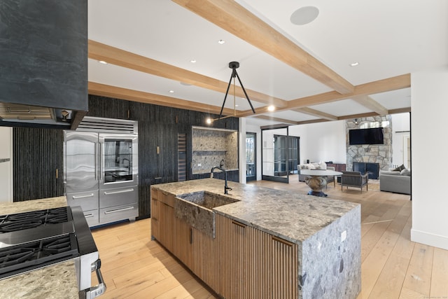 kitchen featuring beam ceiling, a large island, sink, light stone counters, and a fireplace